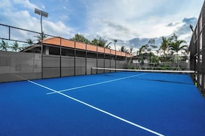 An indoor tennis court with a blue surface, surrounded by a fence, and adjacent to a building with a tiled roof. - Villa Maxime by BaliSuperHost (Bali)