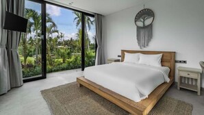 A bedroom with a large bed, a TV, a bedside table, and a view of palm trees through a glass door. - Villa Maxime by BaliSuperHost (Bali)