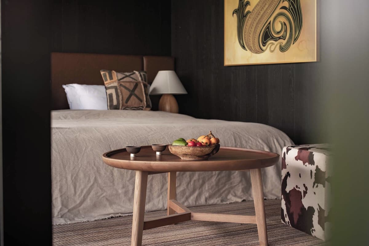 Une chambre d’hôtel avec un lit, une table de chevet sur laquelle se trouve un bol de fruits, une lampe et un élément décoratif mural.
