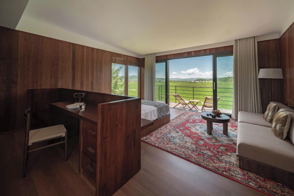 Une chambre à coucher comprenant un lit, un bureau, une chaise, un canapé et un balcon avec vue sur la campagne.