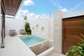 Ein Poolbereich mit zwei Liegestühlen, einer Holztür und einer weißen Wand mit Bögen.