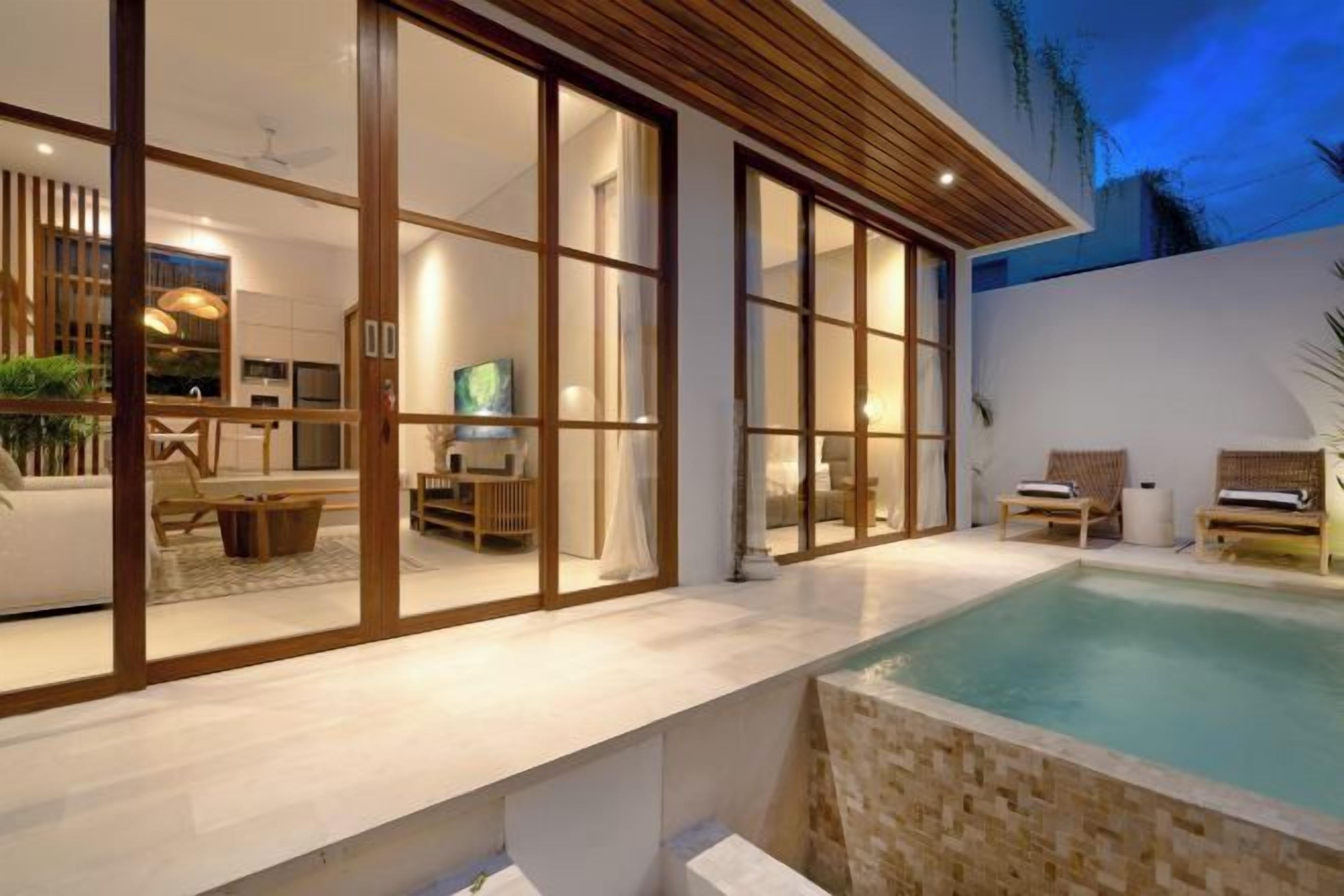A modern house with a swimming pool, large sliding glass doors, and a well-lit interior.