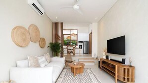 Un salon moderne avec un canapé blanc, une table basse en bois, un téléviseur posé sur un meuble en bois et un tapis à motifs.