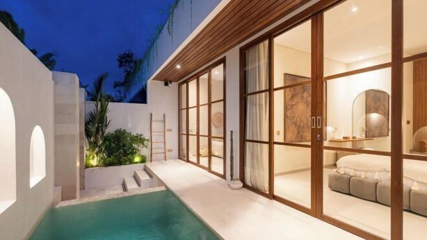 Une maison moderne dotée d’une piscine, de grandes portes-fenêtres coulissantes donnant sur une chambre, et d’un petit espace extérieur agrémenté de plantes.