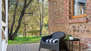 A wooden deck with a black chair and a small table with a plant. - Orchard Cottage—A Leafy Peaceful Retreat with Spa (Lenswood)