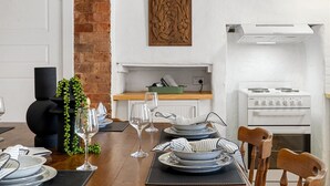 A dining area with a wooden table set for a meal, a white stove, and a brick wall. - Orchard Cottage—A Leafy Peaceful Retreat with Spa (Lenswood)