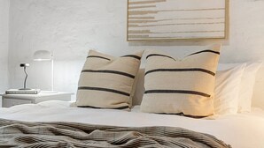 A bedroom with a bed, two pillows with black stripes, a bedside lamp, and a framed abstract artwork on the wall. - Orchard Cottage—A Leafy Peaceful Retreat with Spa (Lenswood)