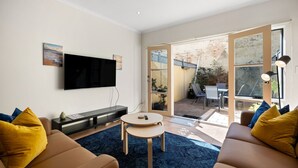 En stue med et fladskærms-TV, en sofa, et sofabord og udsigt til en udendørs terrasse.