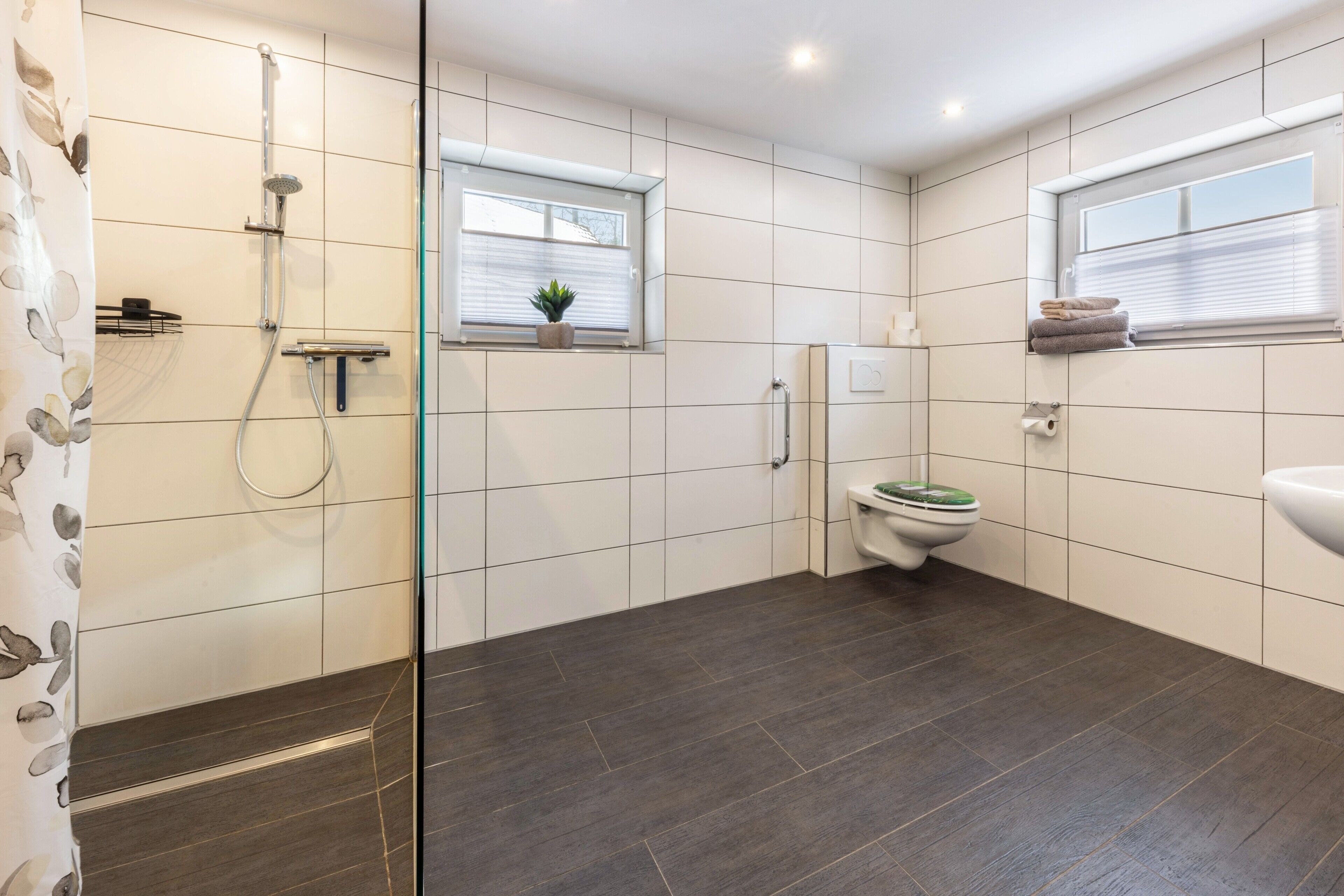 Een moderne badkamer met douche, toilet en wastafel, met betegelde wanden en donkere vloer.