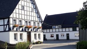 A traditional half-timbered building with a steeply pitched roof, a central entrance, and flower boxes on the windowsills.