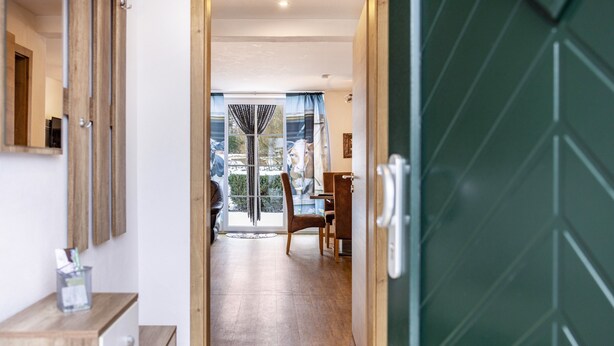 A hallway leading to a dining area with a view of the outdoors, a wooden floor, and a green door.
