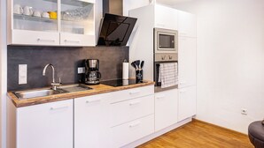 A modern kitchen with white cabinets, a stainless steel sink, a built-in oven, and a coffee maker.