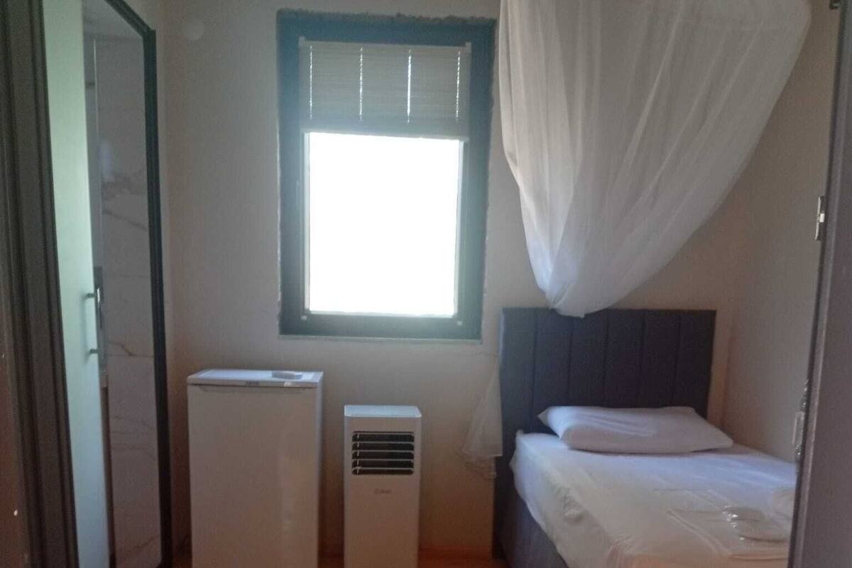 A bedroom with a bed, a window with blinds, and two air conditioning units.