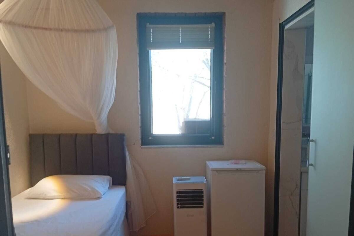 A small, narrow room with a bed, a window, and a small air conditioning unit.