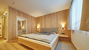 A bedroom with a wooden bed, two bedside tables with lamps, a large mirror, and a wooden wardrobe. - Chalet Almglück by we rent (Saalbach-Hinterglemm)