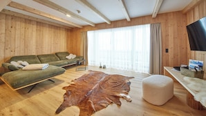 A cozy room with wooden walls, a green sofa, a leather rug, and a television on a wooden table. - Chalet Almglück by we rent (Saalbach-Hinterglemm)