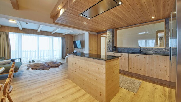 A modern kitchen with wooden cabinetry, a large island, and a stone backsplash. - Chalet Almglück by we rent (Saalbach-Hinterglemm)