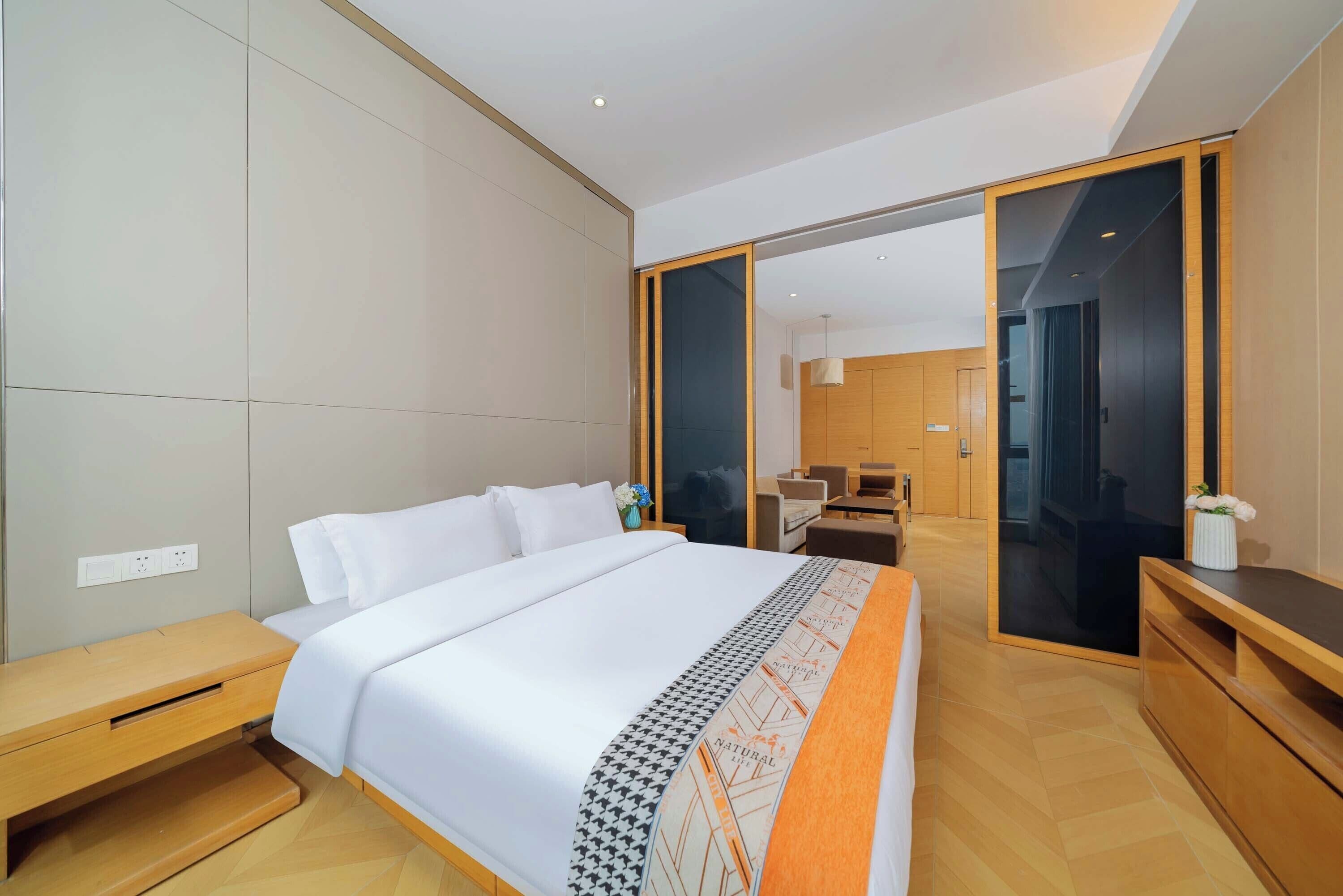 A modern hotel room with a large bed, wooden flooring, a desk, and a wardrobe.
