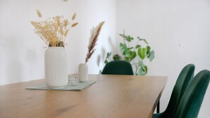 Une table en bois sur laquelle se trouve un vase blanc contenant des plantes séchées, un verre et une petite bougie.
