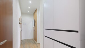 Un couloir avec une porte en bois, un miroir et une armoire blanche à rayures horizontales noires.