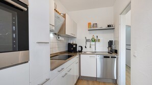 Une cuisine compacte avec des meubles blancs, un lave-vaisselle en acier inoxydable, une machine à café et un four encastré.