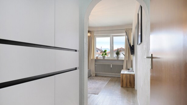 Un couloir donnant sur un balcon, avec un radiateur et une petite table sur laquelle est posée une plante.