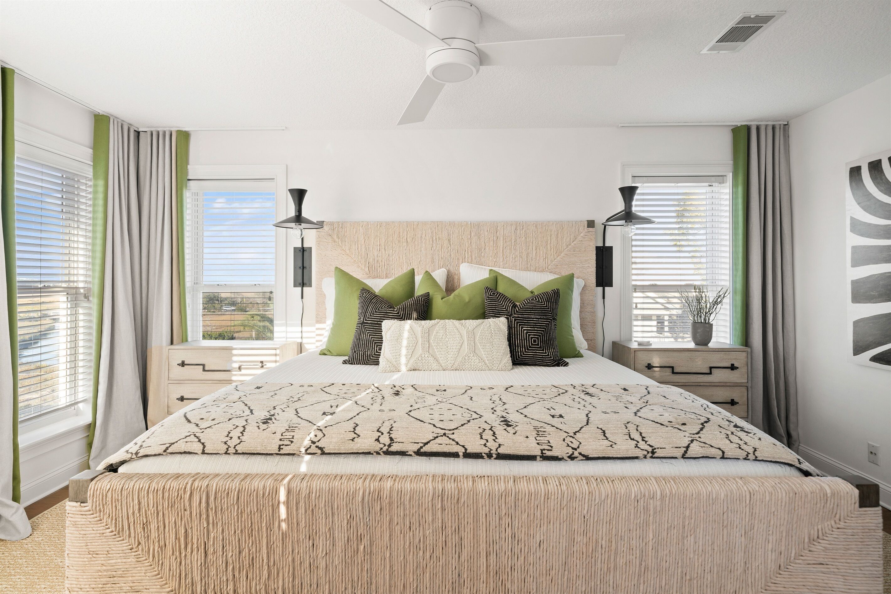 A bedroom with a bed, two bedside tables, a ceiling fan, and a window with curtains.