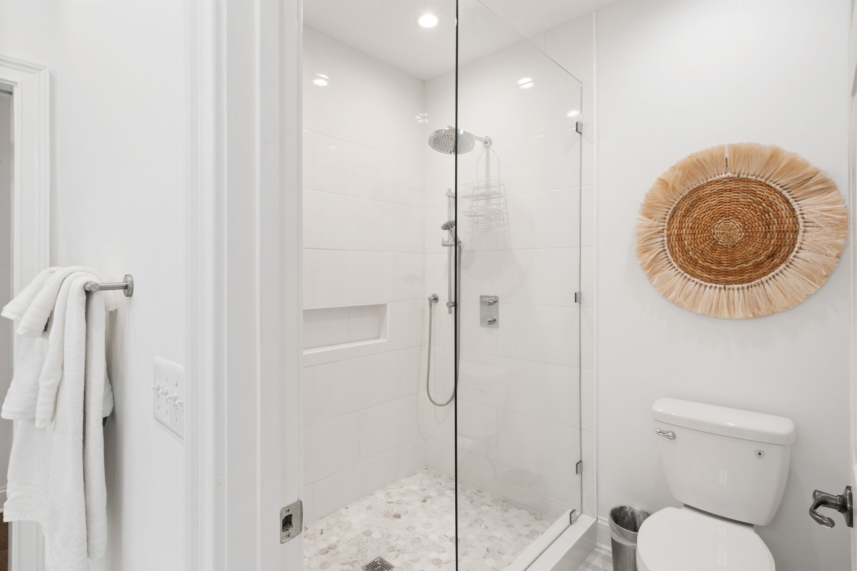 Ein modernes Badezimmer mit einer gläsernen Duschkabine, einer Toilette und einer dekorativen Wandgestaltung aus gewebtem Material.