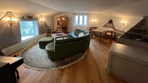 Et hyggeligt loftsværelse med en grøn sofa, et træspisebord og et lille køkkenområde.