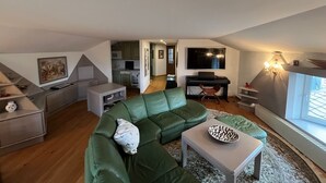 En moderne loftlejlighed med en grøn sofa, et spisebord, et fladskærms-TV og et køkkenområde.