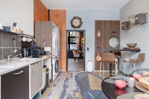 A modern kitchen with a built-in washing machine, a dining area with a round table, and a bar area with stools.
