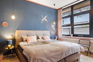 A bedroom with a large bed, bedside lamps, a radiator, and a window with a view.