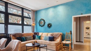 Uma sala de estar com sofá, cadeiras, mesa de centro, uma cadeira de madeira e uma parede decorada com duas guirlandas.