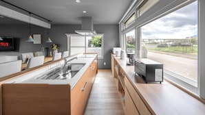 A modern kitchen with a large island, built-in appliances, and a view of the street through large windows. - THE ARBANO (Furano)
