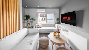 A modern living room with a white sofa, a round wooden table, and a mounted TV displaying "NETFLIX". - THE ARBANO (Furano)