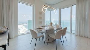 A modern dining area with a round table, four chairs, and a view of the sea through large windows. - La Vie Residence - JBR Dubai (Dubai)