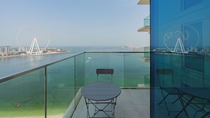 A balcony with a glass railing overlooking a body of water, a Ferris wheel in the distance, and a table with a chair. - La Vie Residence - JBR Dubai (Dubai)