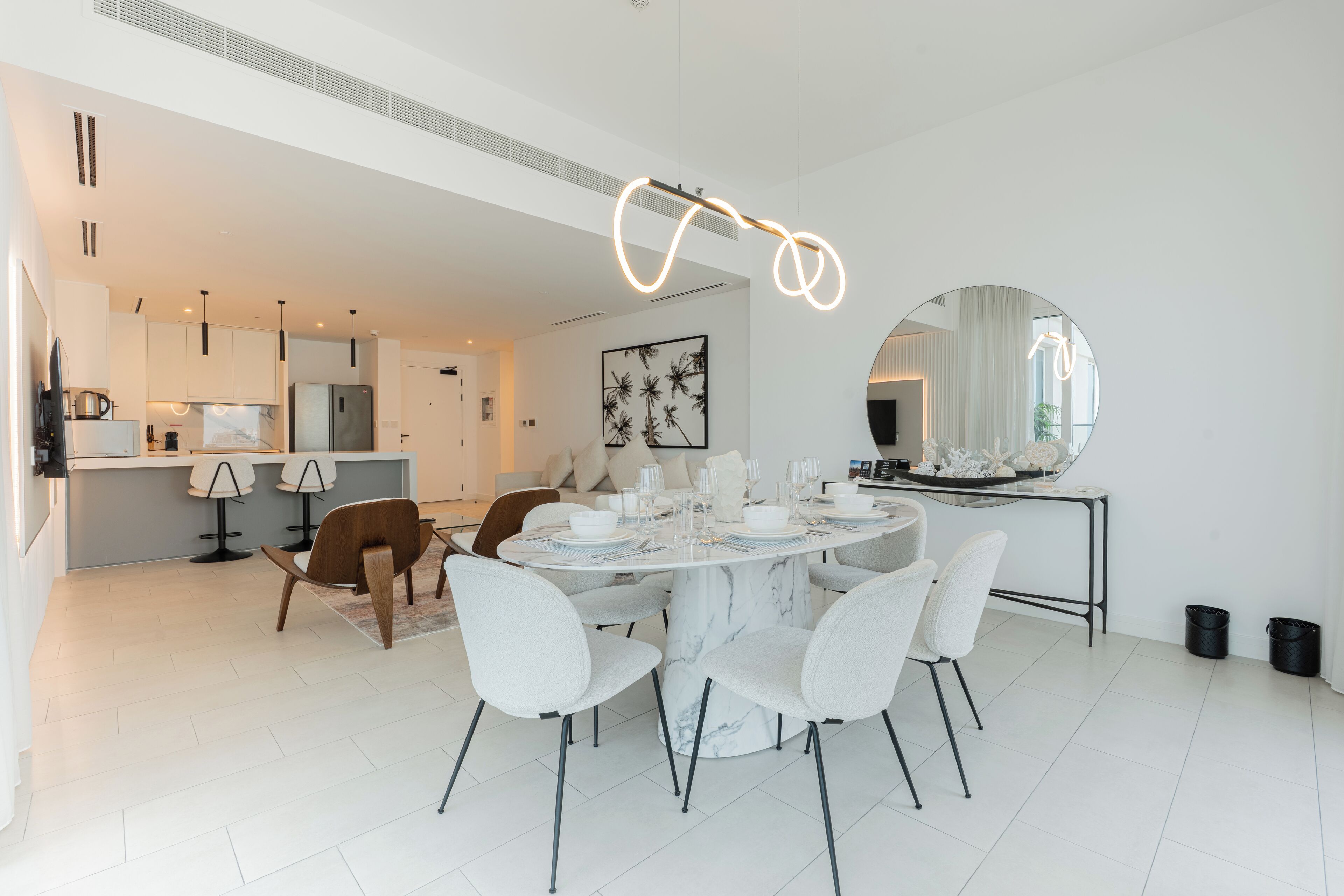A modern kitchen with white cabinets, a marble island, and a dining area with a round table and white chairs.