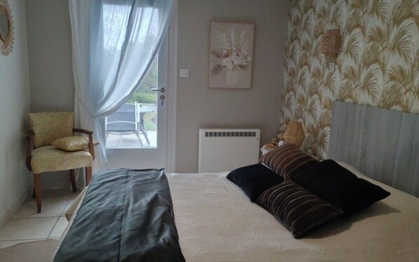 A bedroom with a bed, a chair, a radiator, and a door leading to a balcony. - COLUMBIA (Concorès)