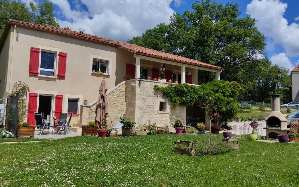 Une maison à deux étages avec des volets rouges, un mur en pierre et un jardin agrémenté de plantes en pot.