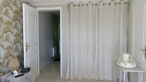 A bathroom with a shower curtain, a bedside table with a lamp, a remote control, and a pitcher on a small table. - COLUMBIA (Concorès)