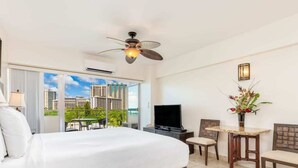 A hotel room with a large bed, a television, a desk with a chair, and a balcony with a view of buildings.