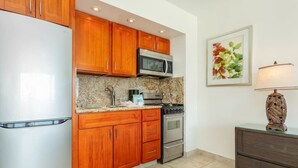 A kitchen with wooden cabinets, a stainless steel refrigerator, a microwave, a stove, and a countertop with a granite backsplash.