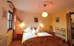 A bedroom with a wooden bed, a nightstand, a dresser, a window with curtains, and a ceiling light fixture.