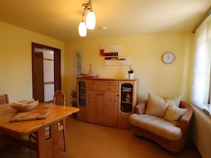 Un salon chaleureux avec une table à manger en bois, un canapé, un meuble avec des étagères et une horloge murale.