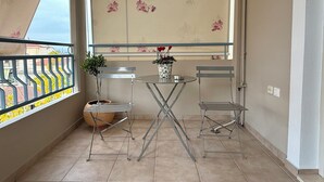 A balcony with a metal table and chairs, a potted plant, and a window with floral wallpaper. - Domus Philippi–Spacious Stay the Heart of Larisa, Perfect for Families & Friends (Larisa)