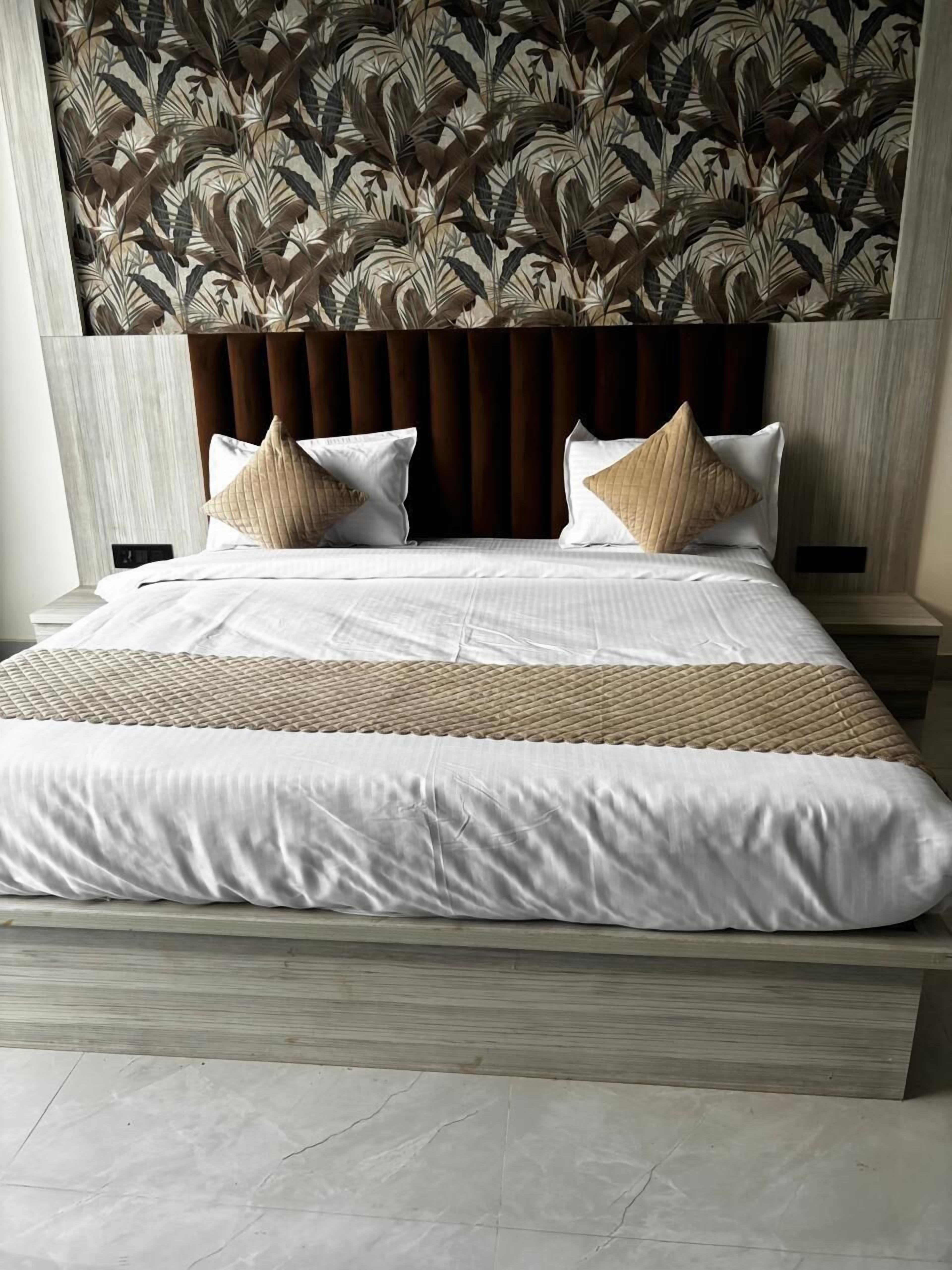 A neatly made bed with a patterned headboard, two pillows, and a wooden bedside table.