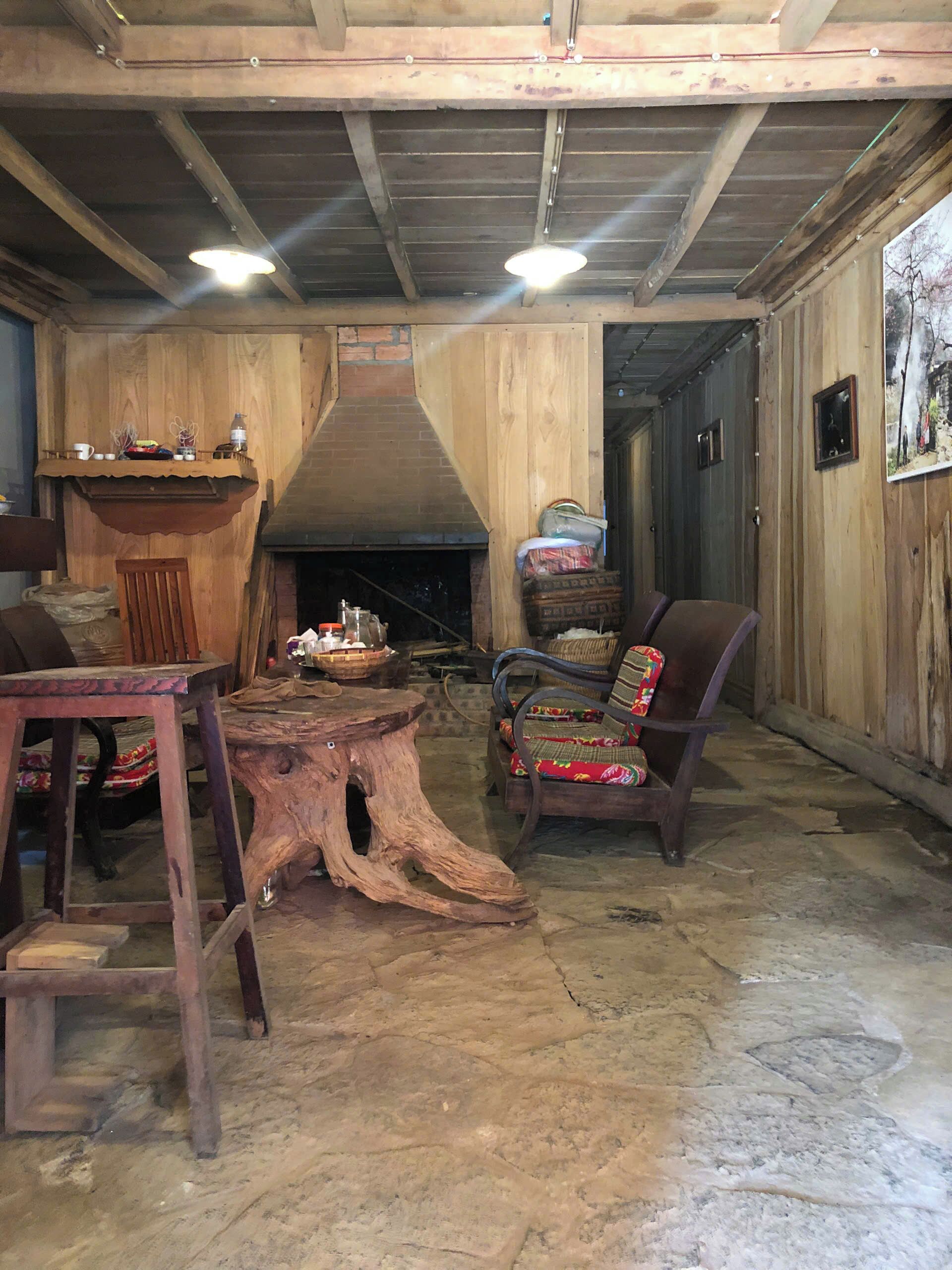 A rustic interior with a stone floor, wooden furniture, a fireplace, and a wooden ceiling.