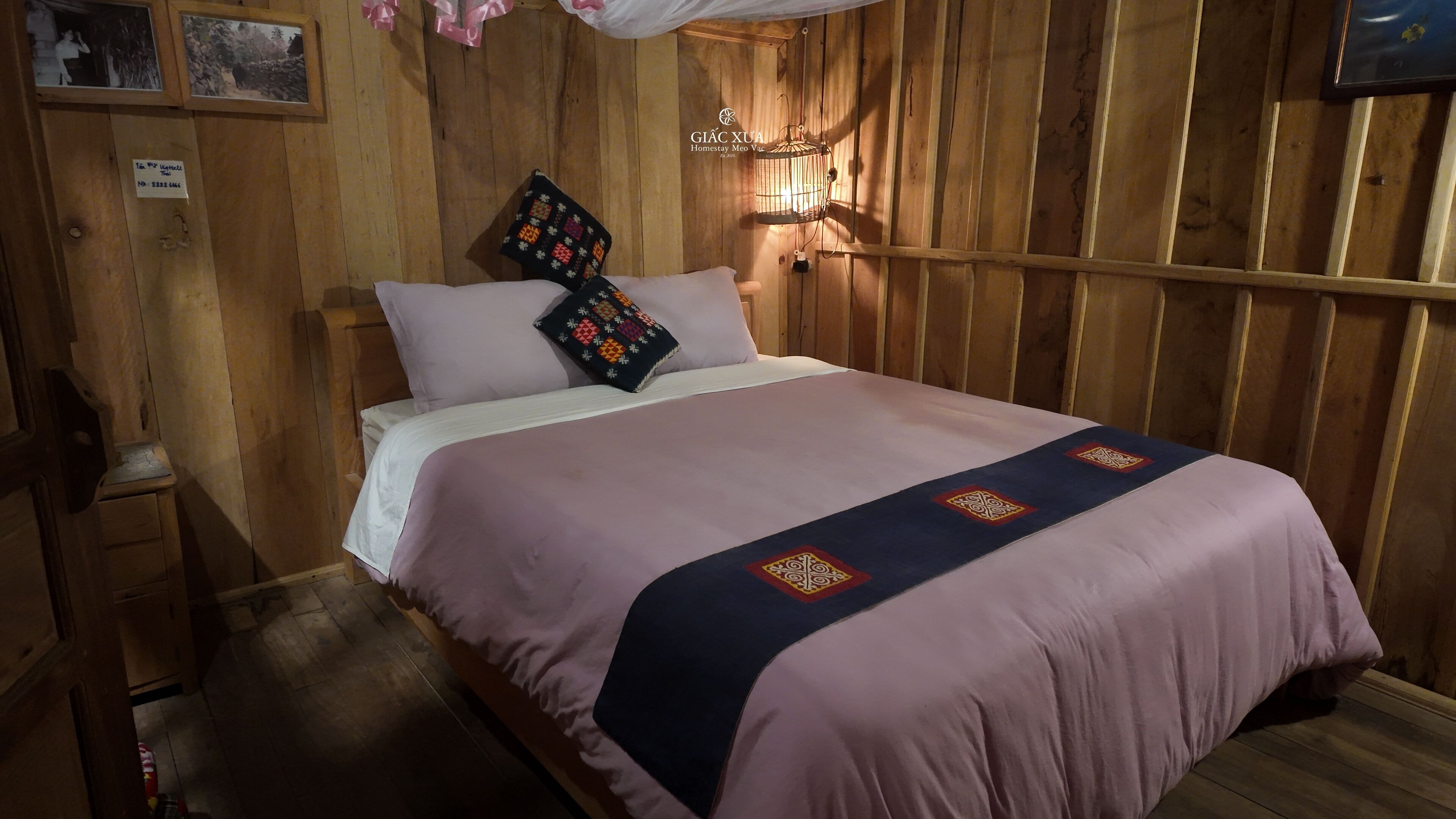 Una habitación de madera con cama, mesita de noche, luz empotrada en la pared y lámpara colgante.