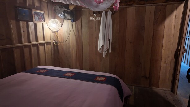 Une pièce en bois avec un lit, un ventilateur fixé au mur, un luminaire et un porte-serviettes.